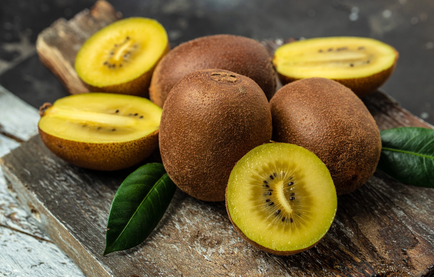 Kiwis golden entiers et coupés en deux montrant leur chair jaune, sur une planche en bois rustique