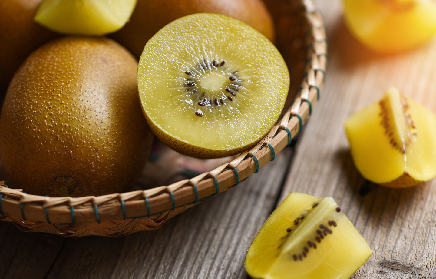 Kiwis golden entiers et coupés en tranches dans un panier en osier, sur une table en bois